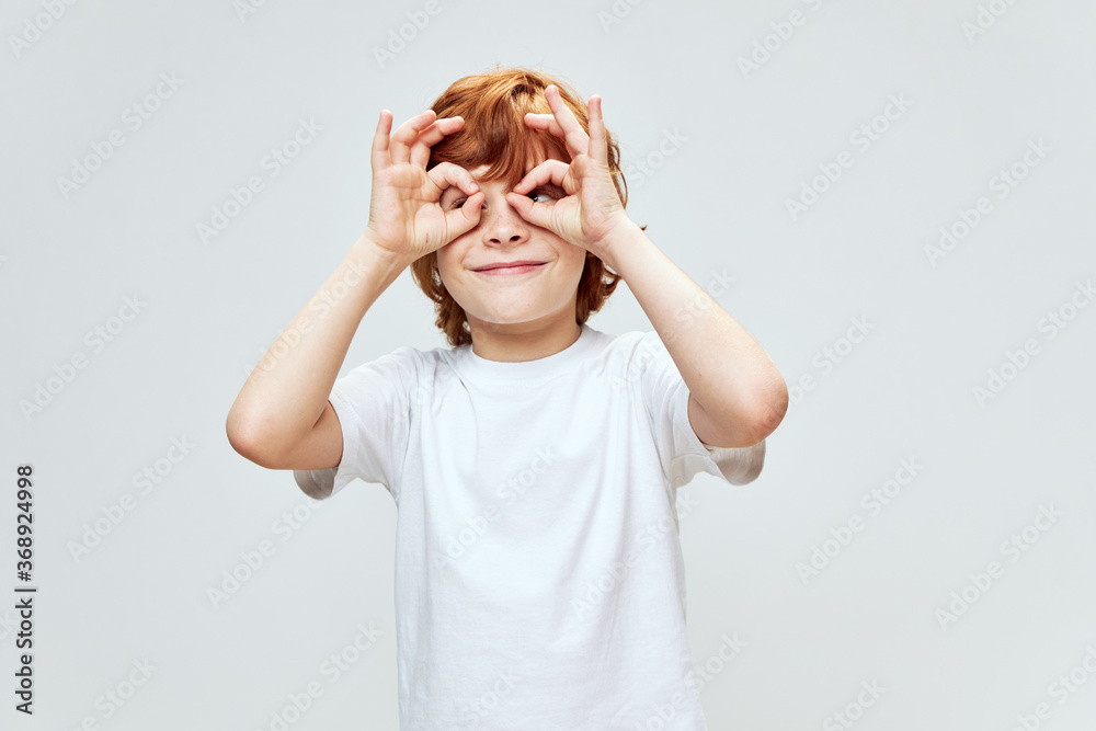 Cheerful red-haired boy holding hands near his face in the form of a mask lifestyle white t-shirt Cheerful red-haired boy holding hands near his face in the form of a mask lifestyle white t-shirt