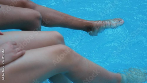 Wallpaper Mural Two barefoot tanning young model sitting poolside joy sunlight testing blue water kicking shaking foot in public pool make beautiful splashes big waves in rest exotic trip tourist resort, closeup view Torontodigital.ca