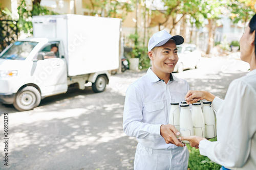 Smiling milkman deliverying milk bottles to pretty female customer
