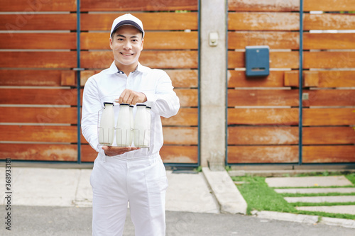 Happy yuong Asian milkman offering fresh milk in glass bottles