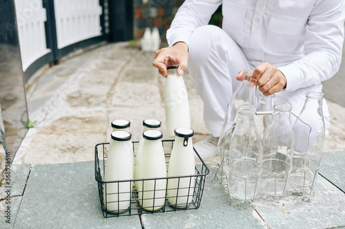Milkman putting glass milk bottles in wire crane and taking back empty bottles