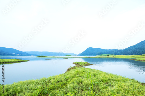 Peaceful and beautiful lake and green field background blue sky,early summer morning landscape.