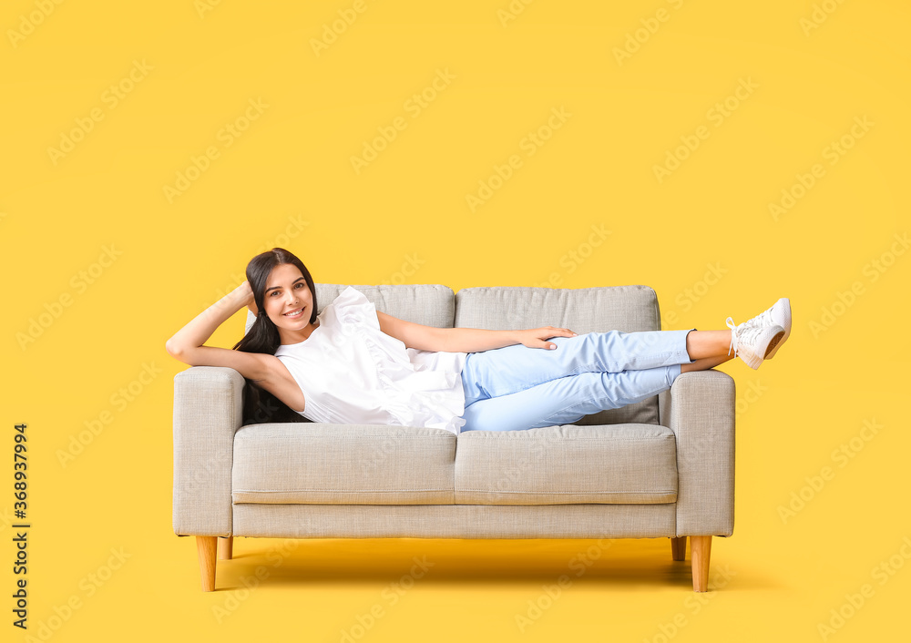 Young woman relaxing on sofa against color background