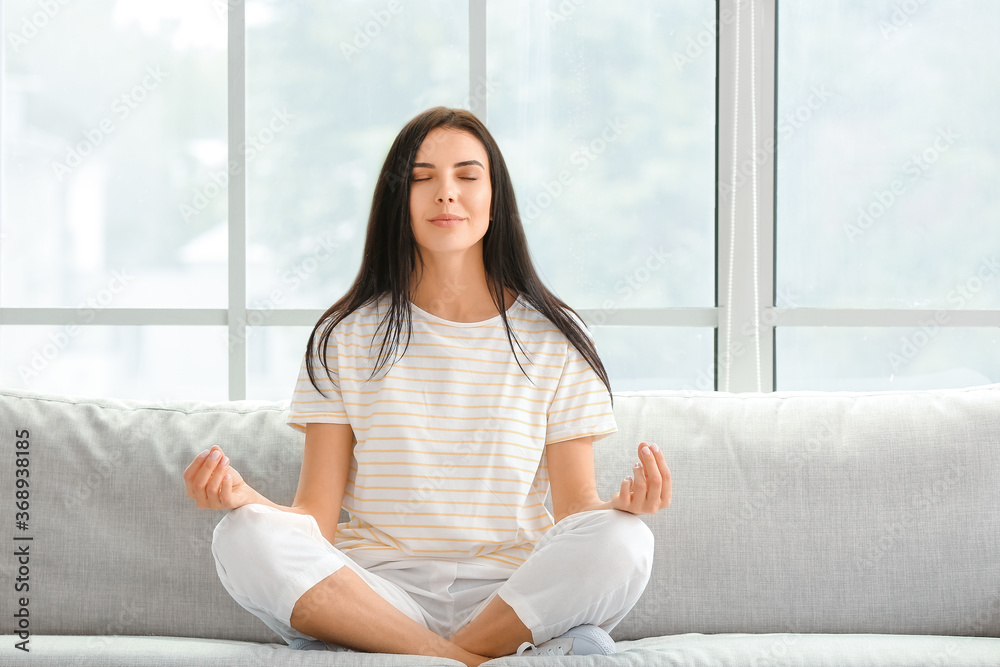 Young woman meditating on sofa at home Young woman meditating on sofa at home