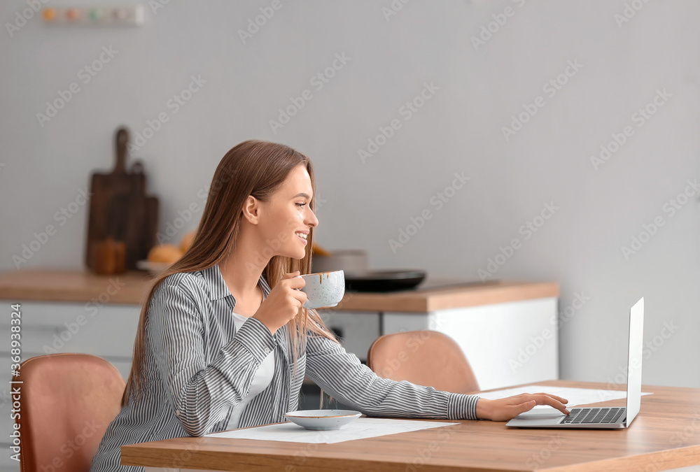 Beautiful young woman with laptop drinking tea at home