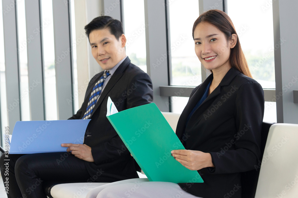 Confident businessman and businesswoman holding file folder during sitting on chair, waiting for job interview in reception hall Confident businessman and businesswoman holding file folder during sitting on chair, waiting for job interview in reception hall