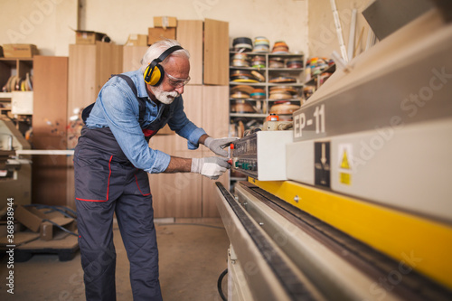 Fotografi Side view of a senior carpenter using an edgebanding machine