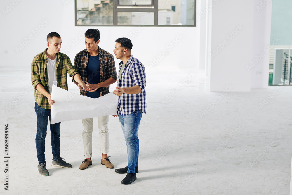 Fototapeta premium Young engineer showing building blueprint to investors at meeting