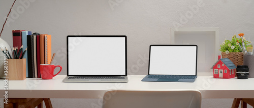 Two blank screen laptop on office desk with books and decorations in home office room