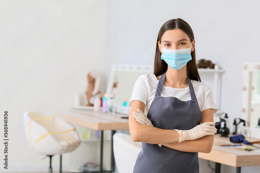 Female hairdresser wearing medical mask in salon during coronavirus epidemic
