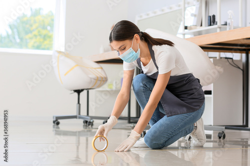 Female hairdresser applying a marking tape on floor in salon during coronavirus epidemic