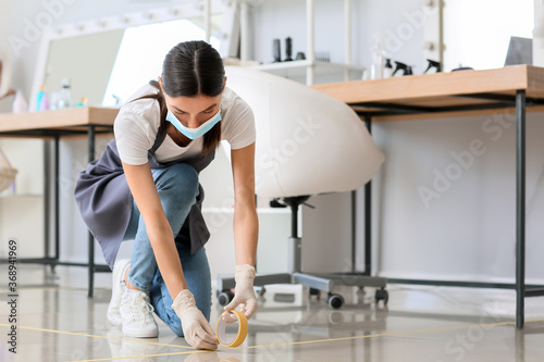 Female hairdresser applying a marking tape on floor in salon during coronavirus epidemic