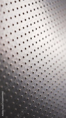 Perforated aluminum surface with many holes. Their ranks go into the distance and form a perspective. Dark vertical wallpaper for mobile phone. Industrial gray metal background. Macro