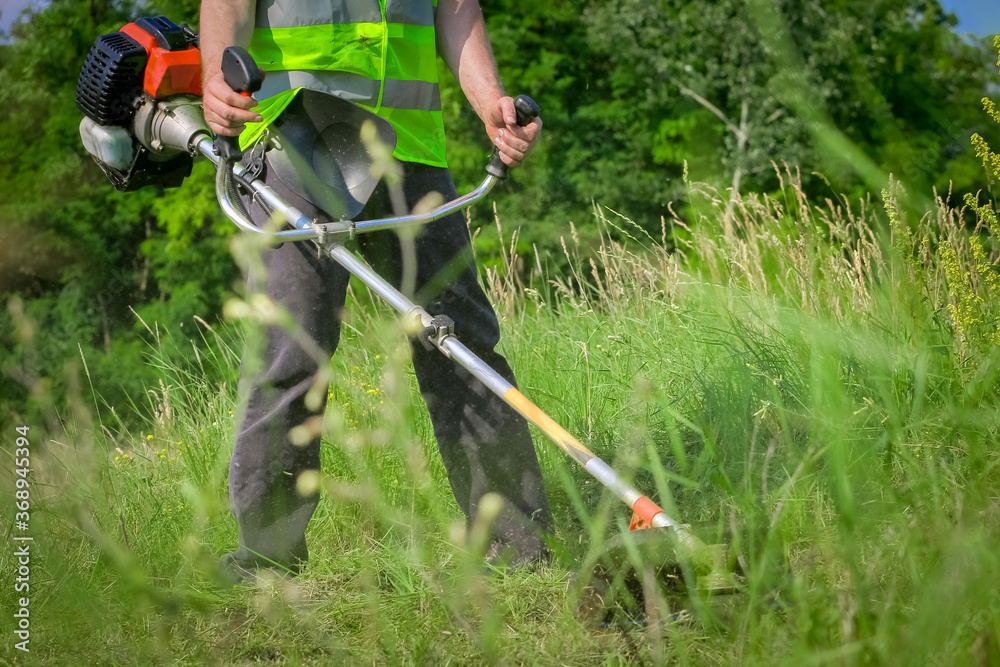 Worker mowing grass with grass trimmer Worker mowing grass with grass trimmer