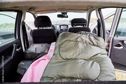 View of a sleeping bag in the cabin of a small car. Overnight in nature near the water of a lake, river, sea or fjord in the cold season. The concept of a trip to nature.