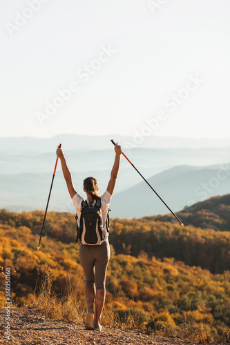 Fototapet Woman happy to hike top of mountain and hold trekking poles
