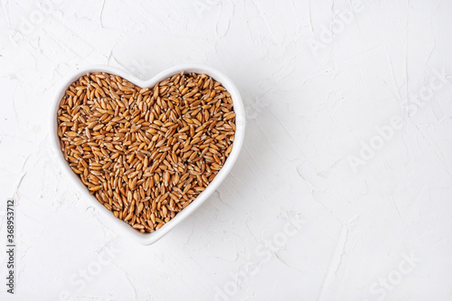 spelt in a white heart-shaped plate, on a white table, top view, cereal