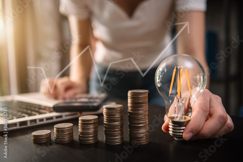 Businessman hand holding lightbulb with using laptop computer and money stack in office. idea saving energy and accounting finance concept in office.