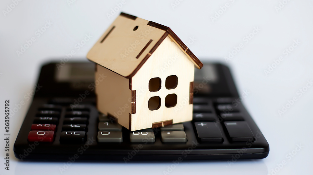 House resting on calculator concept for mortgage calculator, saving for a house House resting on calculator concept for mortgage calculator, saving for a house