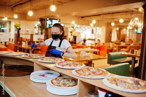 Waiter in protective mask cutting pizza in pizzeria. photo