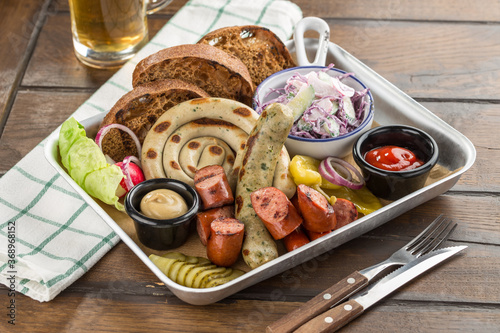 delicious bbq Fried sausages with cabbage, pickles and potato on platter and glass of beer on wooden table