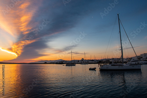 Anchored sailboats with magnificent sunrise with saturated orange and purple bank of clouds in the sky and moonset in Naoussa Village on Paros Island, Greece. © Cleop6atra