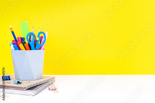 The concept of back to school, education - notebooks, stationery and organizer with multi-colored pens, felt-tip pens, pencils and scissors on a white table on a yellow background with copy space.