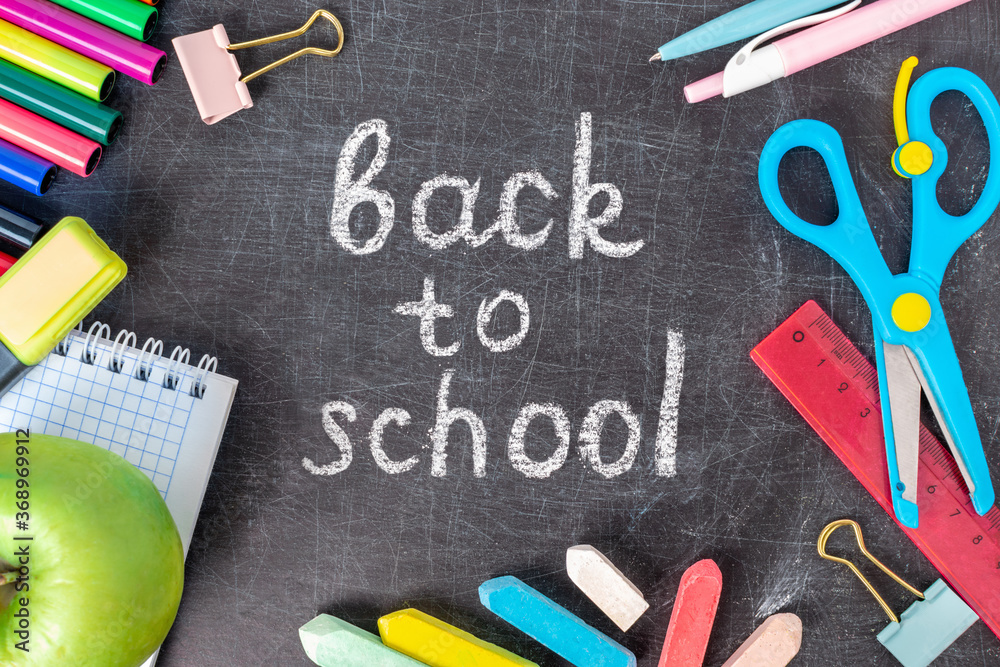 Inscription back to school on the old blackboard with stationery. Colorful crayons, pen, exercise book, scissors,markers and supplies. Chalkboard with pieces of chalk in the classroom. Inscription back to school on the old blackboard with stationery. Colorful crayons, pen, exercise book, scissors,markers and supplies. Chalkboard with pieces of chalk in the classroom.