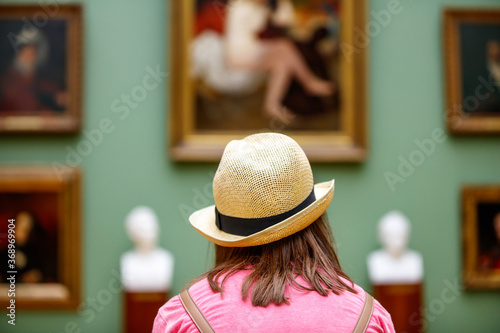 Girl in a hat looks at paintings in a museum photo