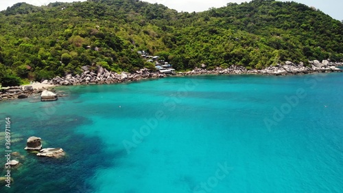 Calm sea near tropical volcanic island. Drone view of peaceful water of blue sea near stony shore and green jungle of volcanic Koh Tao Island on sunny day in Thailand. © Dogora Sun