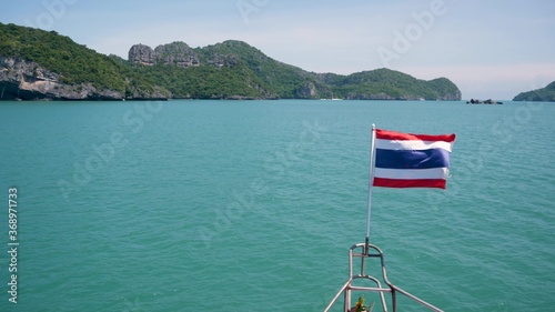 Group of Islands in ocean at Ang Thong National Marine Park. Archipelago in the Gulf of Thailand. Idyllic turquoise sea natural background with copy space. Waving flag as national symbol on the boat.