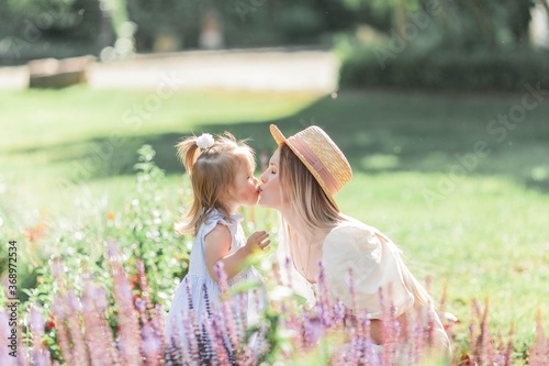 A young mother and her daughter are walking in the flower garden. Roses. Summer.