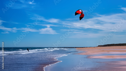 Man kitesurfing or kite boarding sports on Brora beach in the Highlands on a sunny day with blue skies