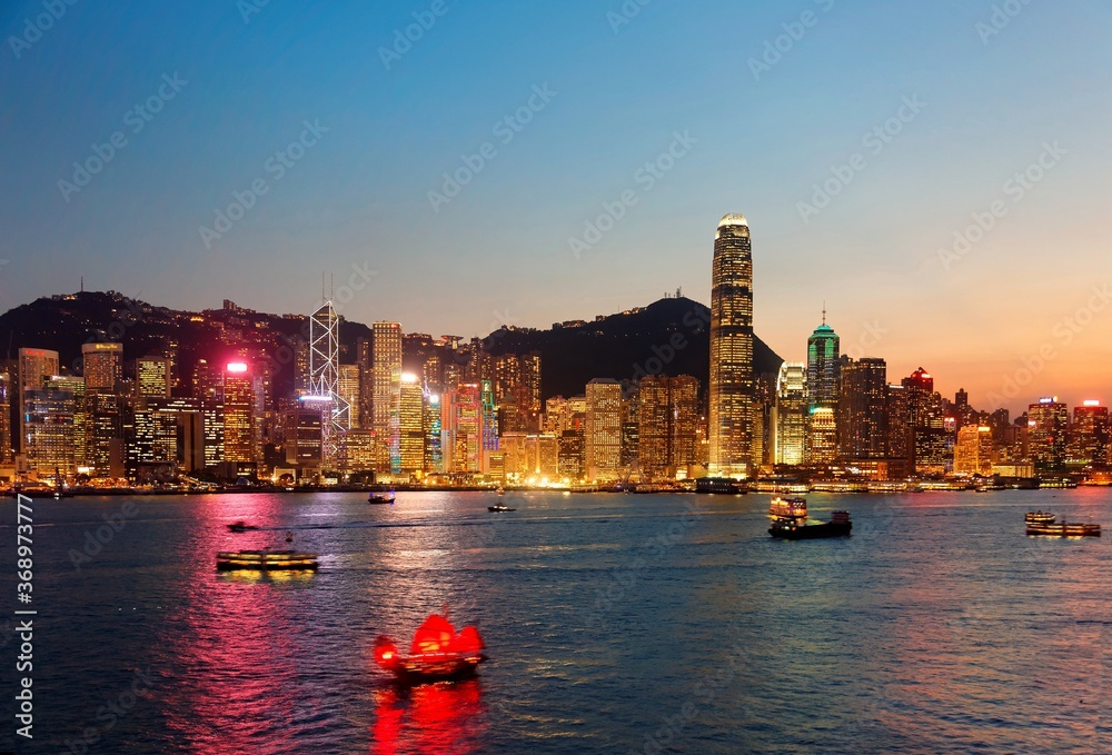 Fototapeta premium Night scenery of Hong Kong with a skyline of crowded skyscrapers by Victoria Harbor, colorful city lights reflected in the water, ferry boats crossing the seaport and Victoria Peak under twilight sky