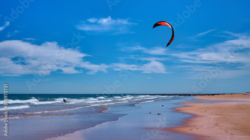 Man kitesurfing or kite boarding sports on Brora beach in the Highlands on a sunny day with blue skies