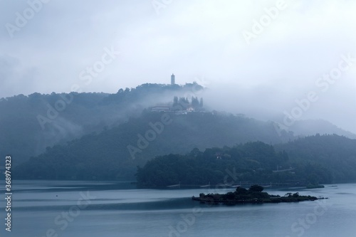 Misty mountains by Sun Moon Lake on a foggy morning, with a pagoda on the distant mountaintop under moody cloudy sky, a famous tourists destination in Nantou, Taiwan (with Chinese Ink Painting effect)
