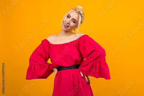 charming blonde girl in a red dress flirts on a yellow studio background