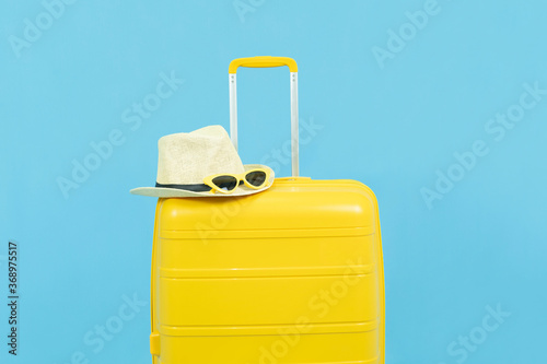 Summer holidays,vacation and travel concept.Yellow Suitcase or luggage sun hat and sunglasses,the reopening of the Tourism after the quarantine on blue background