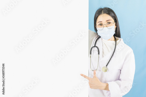 Smart young asian female doctor in lab coat with Medical face mask,white latex medical gloves and stethoscope pointing white blank paper,health care concept