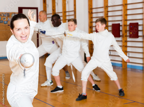 Young positive female training attack movements with rapier at fencing workout