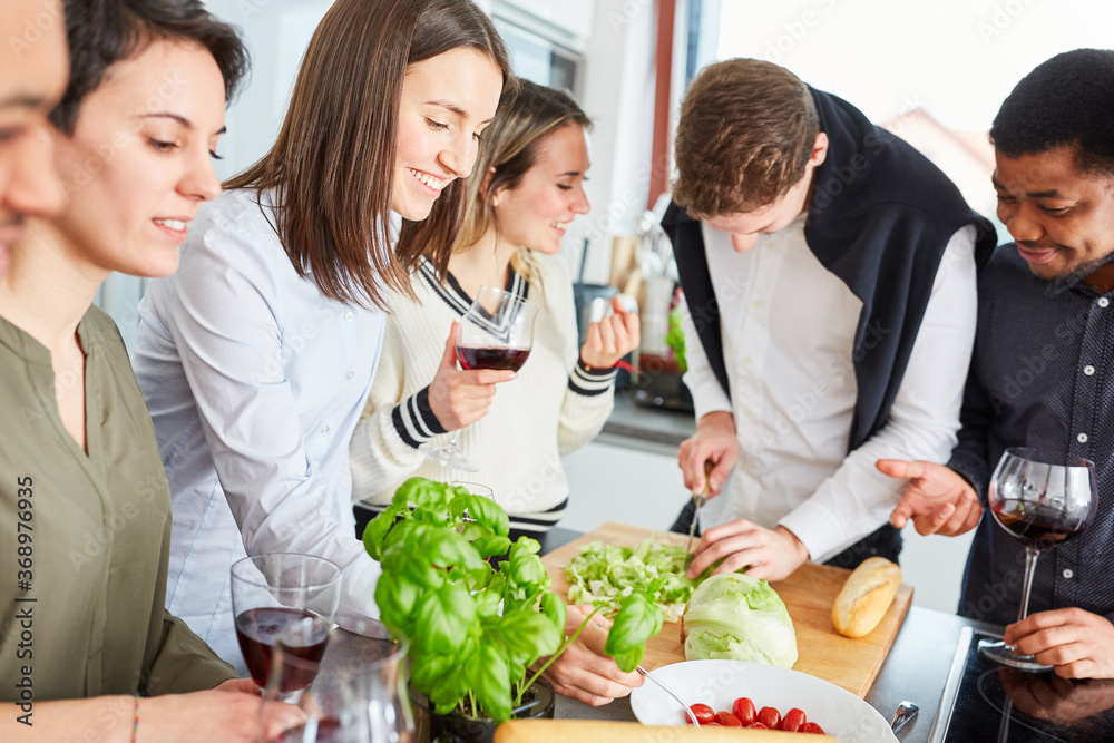 Group of friends in kitchen cutting salad for meal Group of friends in kitchen cutting salad for meal