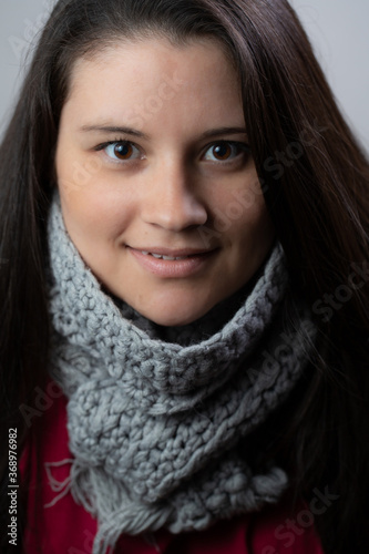 Closeup portrait of a young lady in her thirties. She is wearing winter clothes as a scarf and a coat. She is looking to the camera with a little smile on her face.