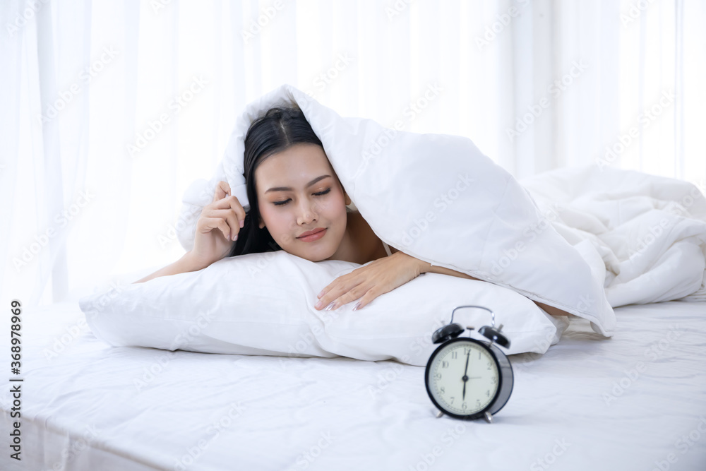 a beautiful Asian woman wake up on white bed in the bedroom, sexy girl unhappy or angry about clock alarm in the morning a beautiful Asian woman wake up on white bed in the bedroom, sexy girl unhappy or angry about clock alarm in the morning