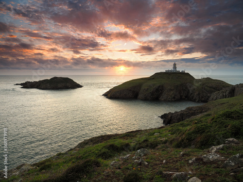 Dramatic sunset view of Strumble Head Lighthouse built by Trinity House in 1908 on the top of the island of Ynys Meicel with orange clouds overhead, Pembrokeshire Coast National Park, Wales, UK
