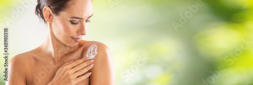 Beautiful young woman applying cream to her shoulder. Skincare spa wellness and cosmetics concept. Blurred green panoramic banner