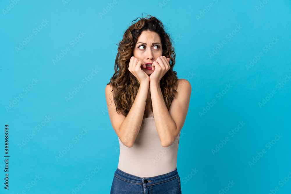 Young caucasian woman isolated on blue background nervous and scared putting hands to mouth Young caucasian woman isolated on blue background nervous and scared putting hands to mouth