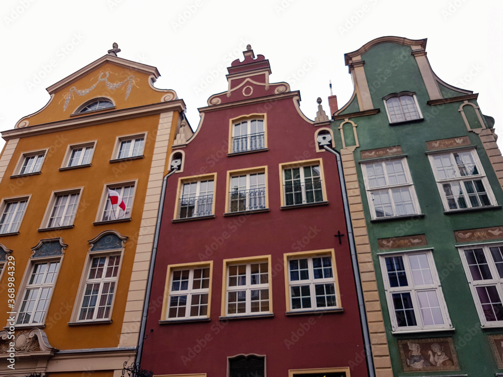 Three colorful old houses in Gdansk with a Polish flag outside a window on a grey day.