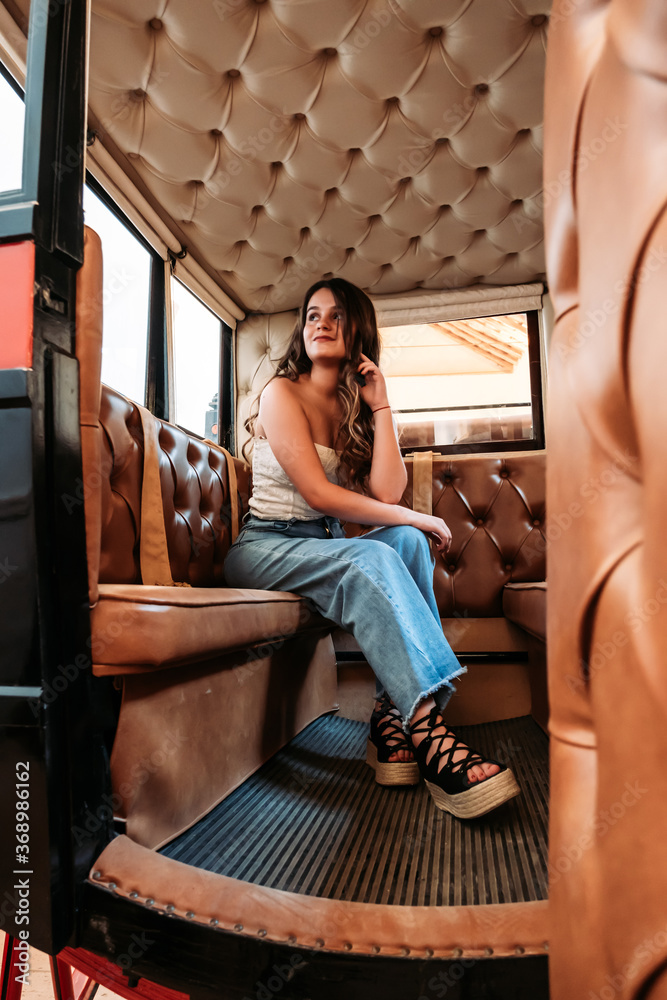 A vertical shot of a caucasian girl sitting inside a compartment with leather seats