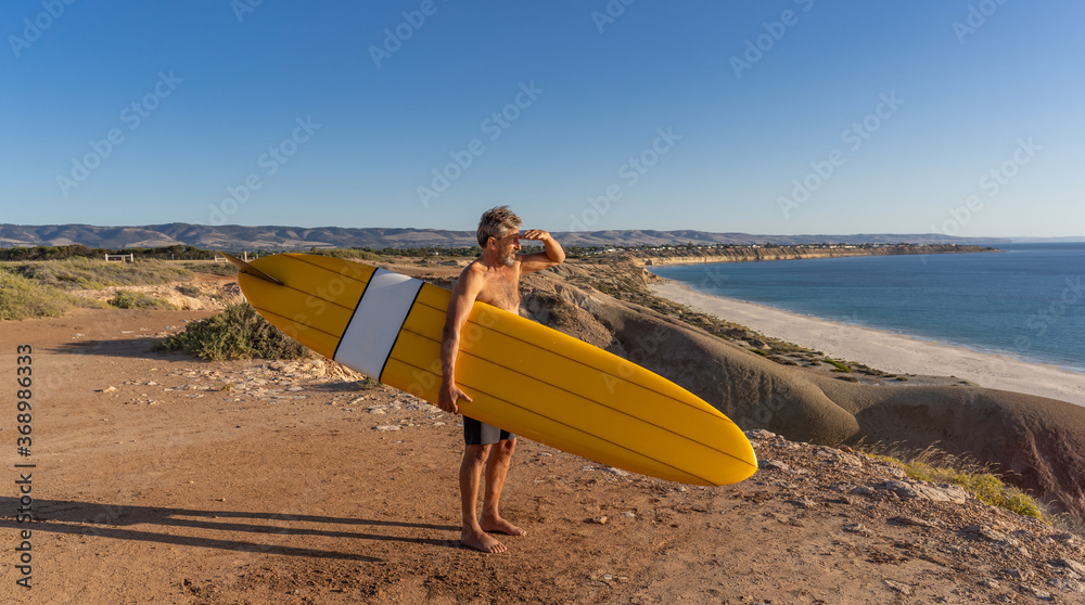 Portrait of mature senior Surfer looking at the ocean with vintage surfboard on an empty beach Portrait of mature senior Surfer looking at the ocean with vintage surfboard on an empty beach