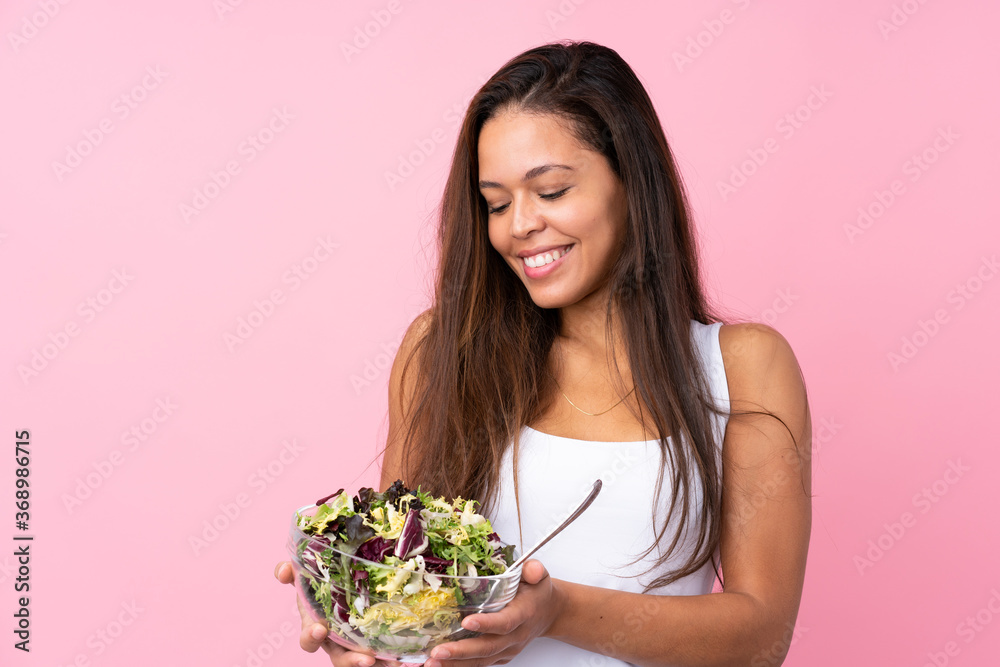 Young Brazilian girl with healthy salad over isolated pink background